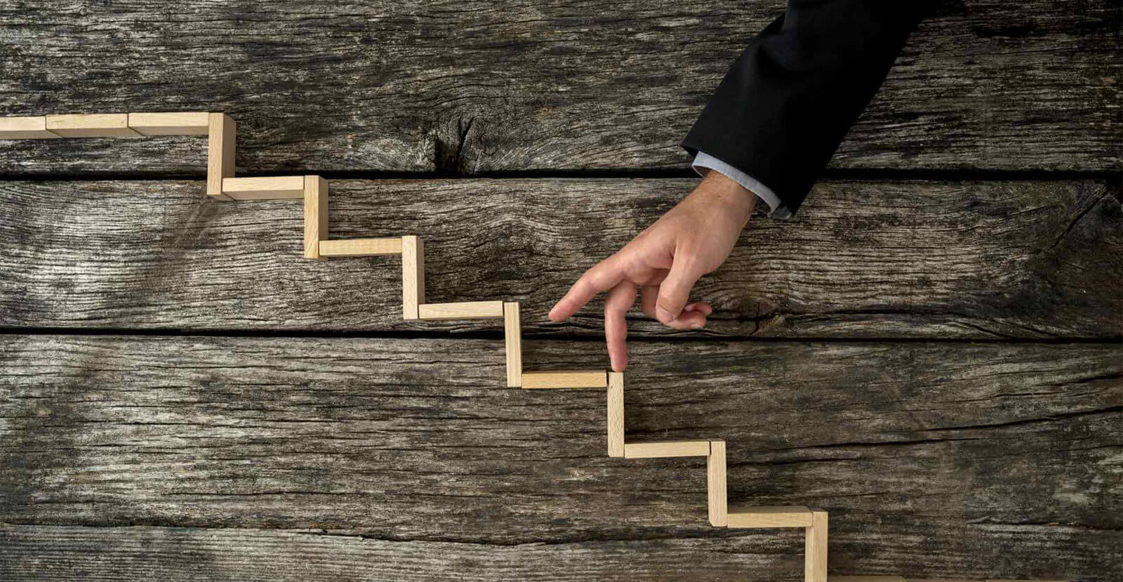 two male fingers tiptoeing up a wooden zigzag staircase model