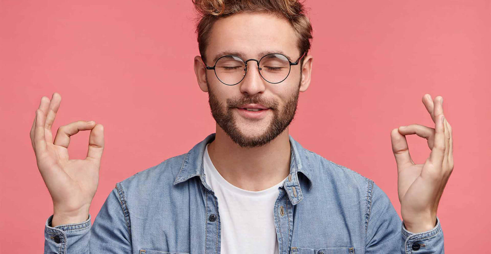 man looking relaxed wearing white tee and blue collared shirt on pink background