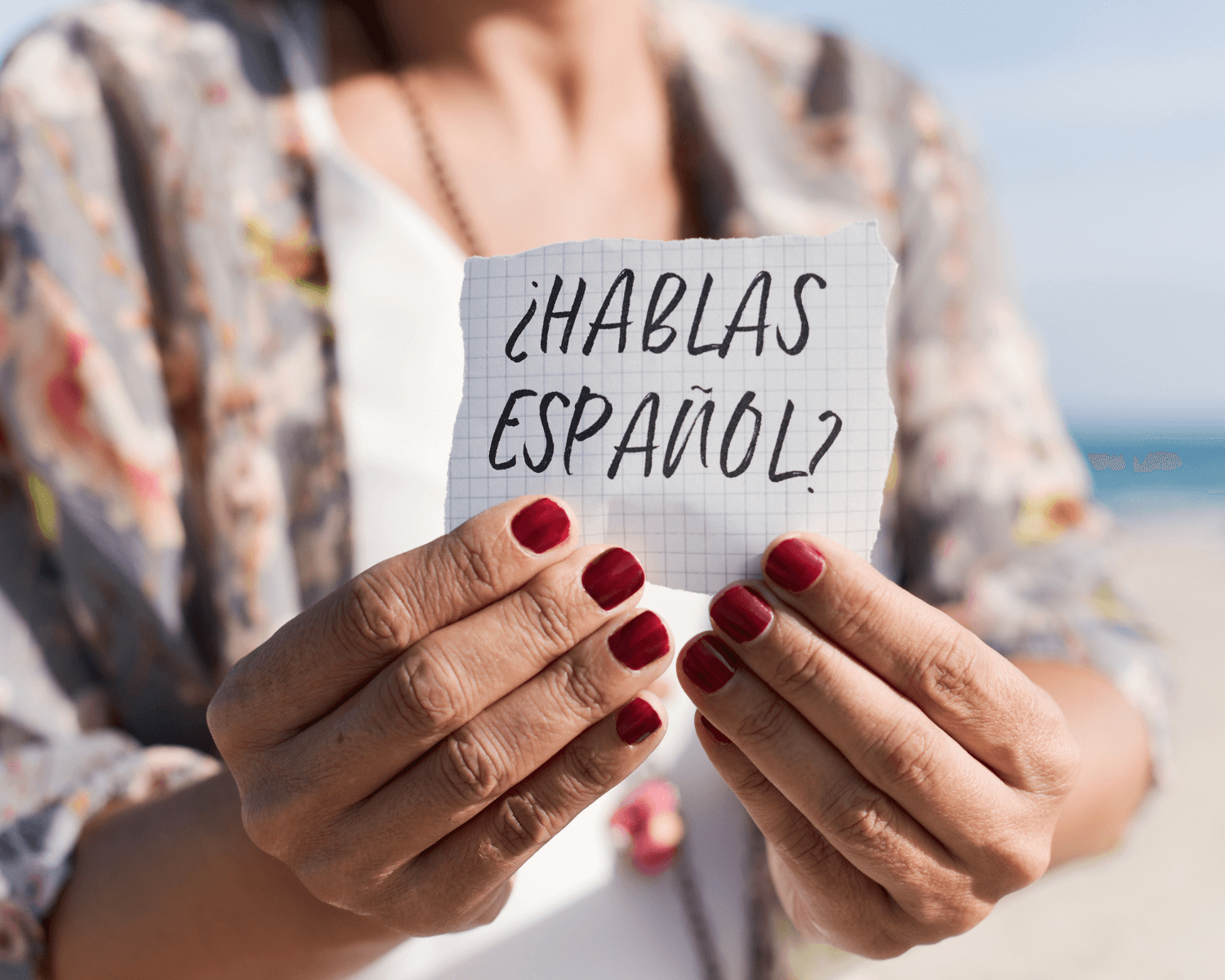 woman wearing white tee shirt and patterned cardigan holding a sign with the words hablas espanol on it