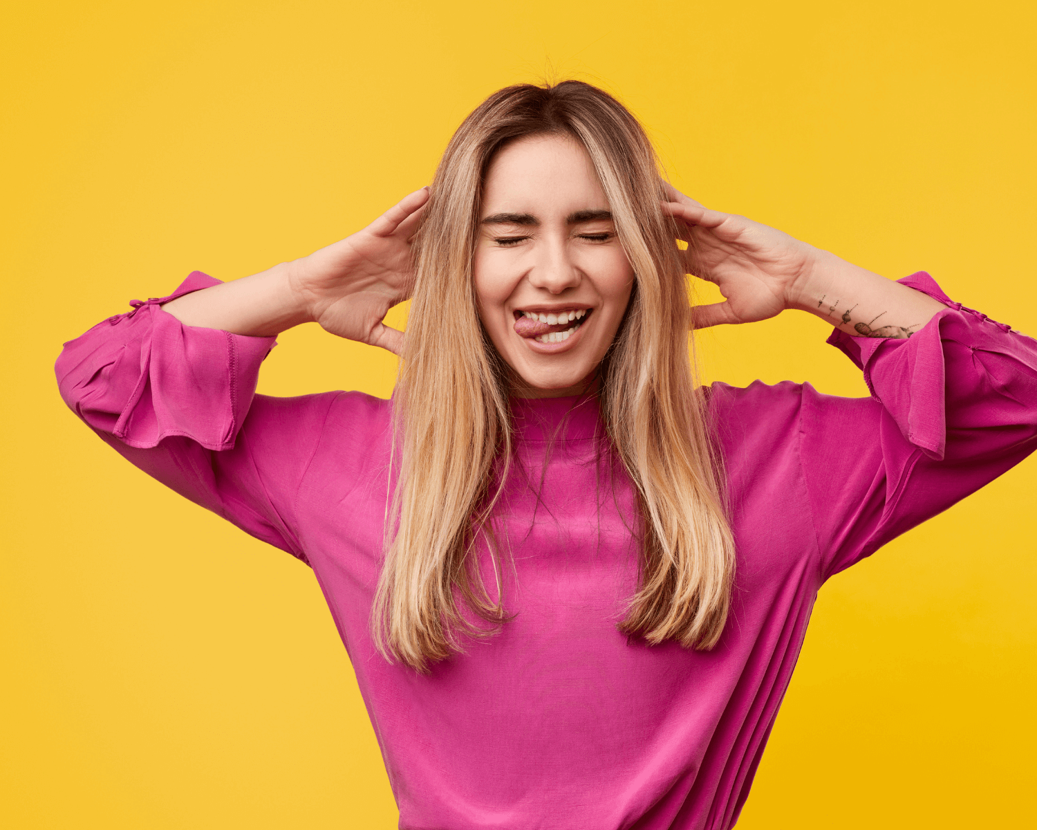 woman in pink sweater biting tongue in front of yellow background